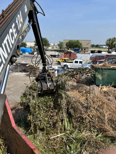 Envirowaste grapple truck claw lifting tree debris on a property cleanup